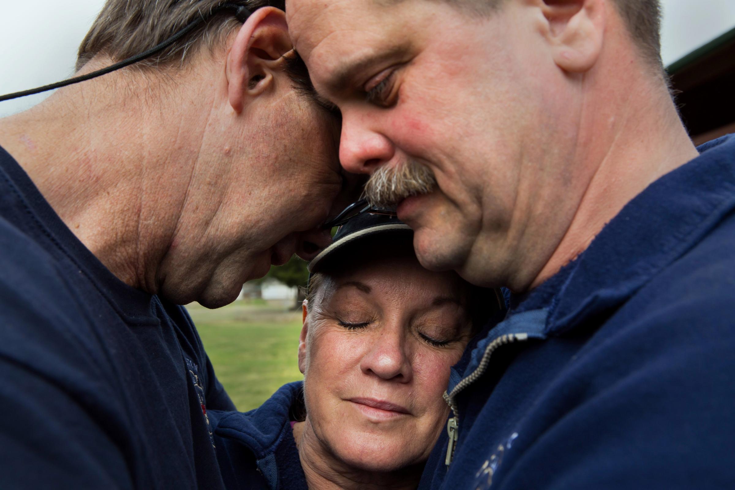 Darrington Fire District 24 volunteer firefighters, Jeff McClelland, left, Jan McClelland, center, and Eric Finzimer embrace each other, March 26, 2014, in Darrington, Wash., after saying a prayer for the victims and survivors of the massive mudslide.