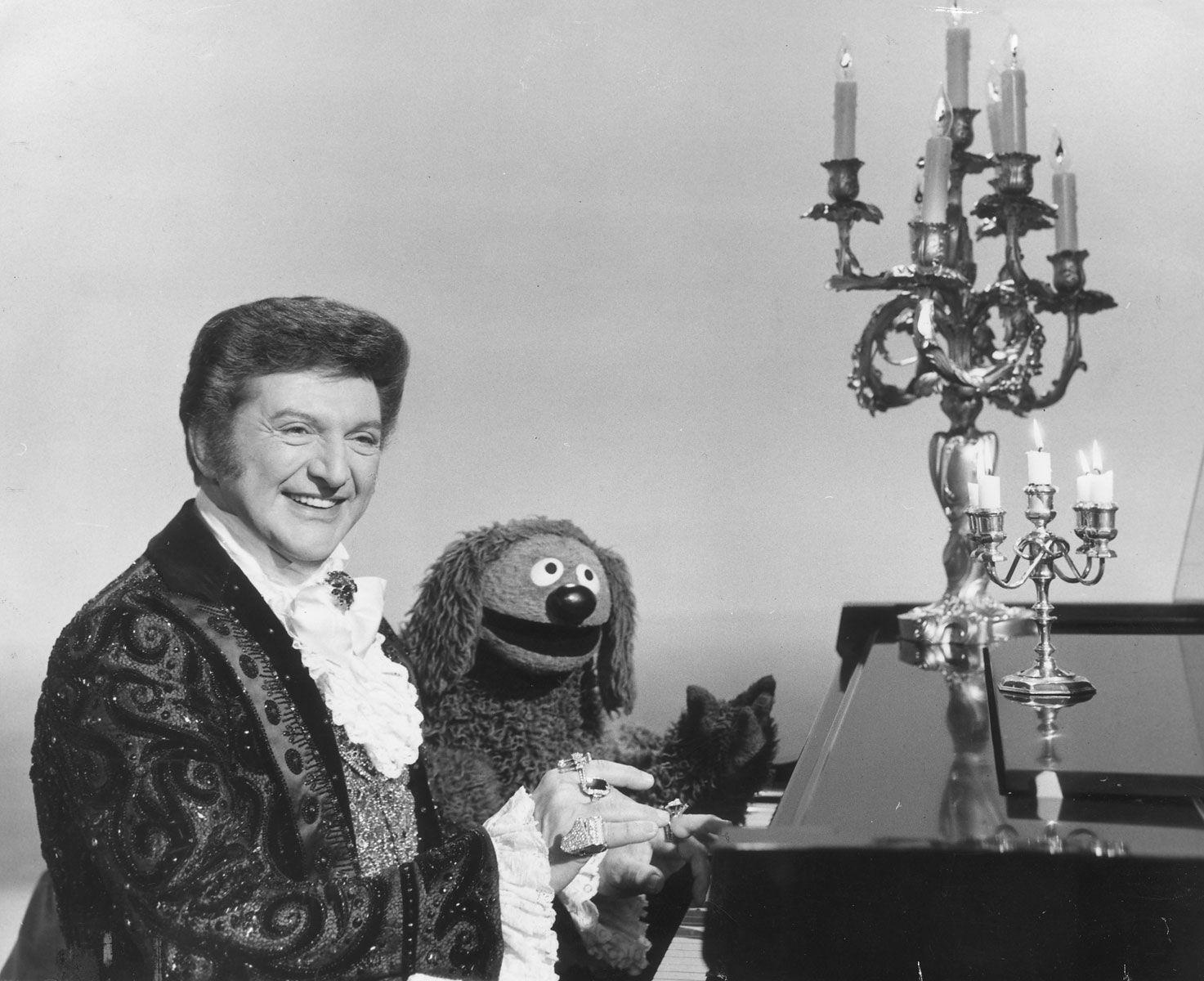 Liberace plays the piano with a little help from Rowlf.