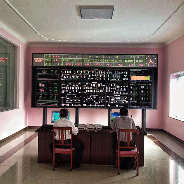 Men sat working beneath a control board at a Pyongyang factory, October 16, 2013.