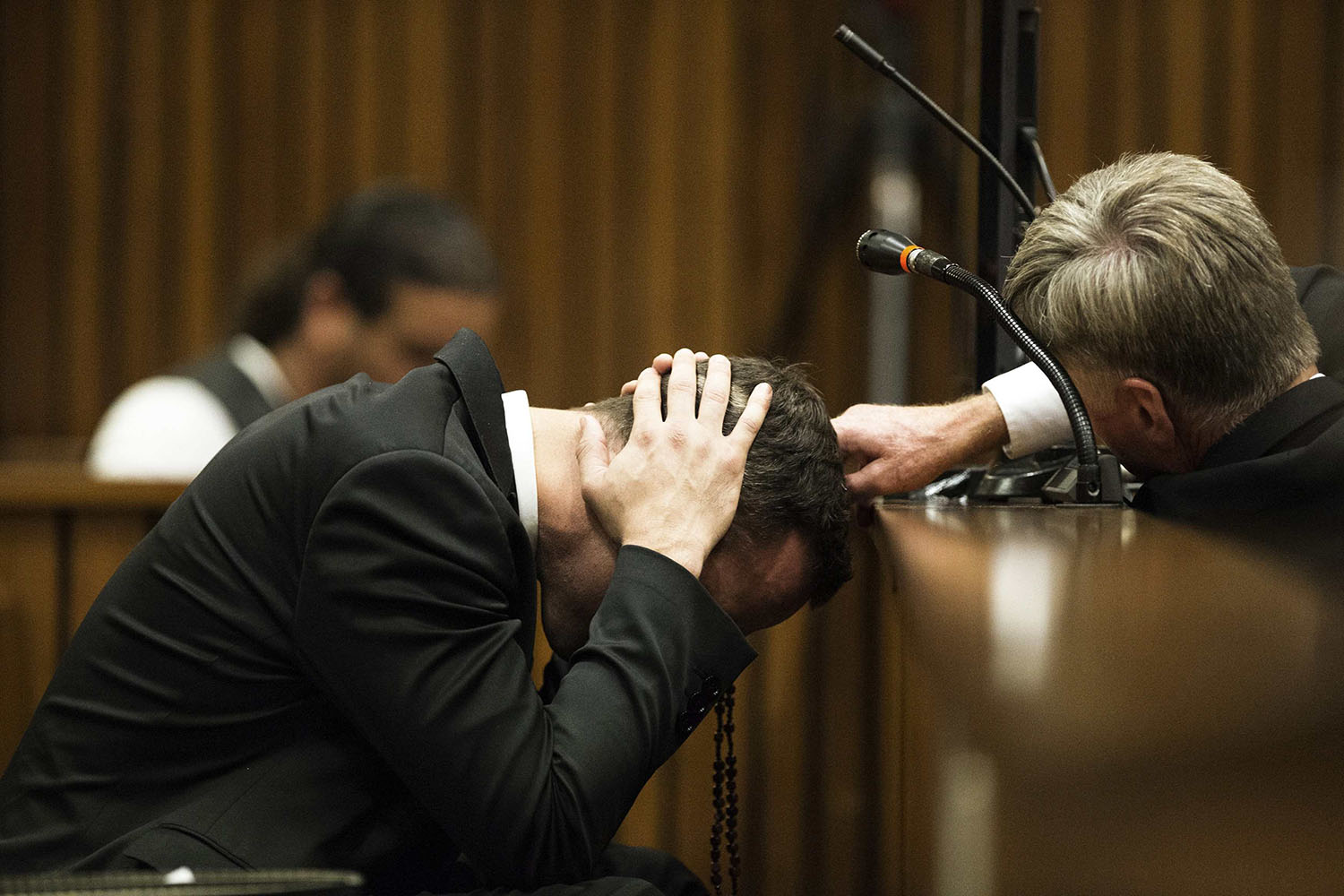 A member of the defence legal team reaches out to Olympic and Paralympic track star Oscar Pistorius as he holds his head while a witness testifies during the fourth day of his trial at the North Gauteng High Court in Pretoria