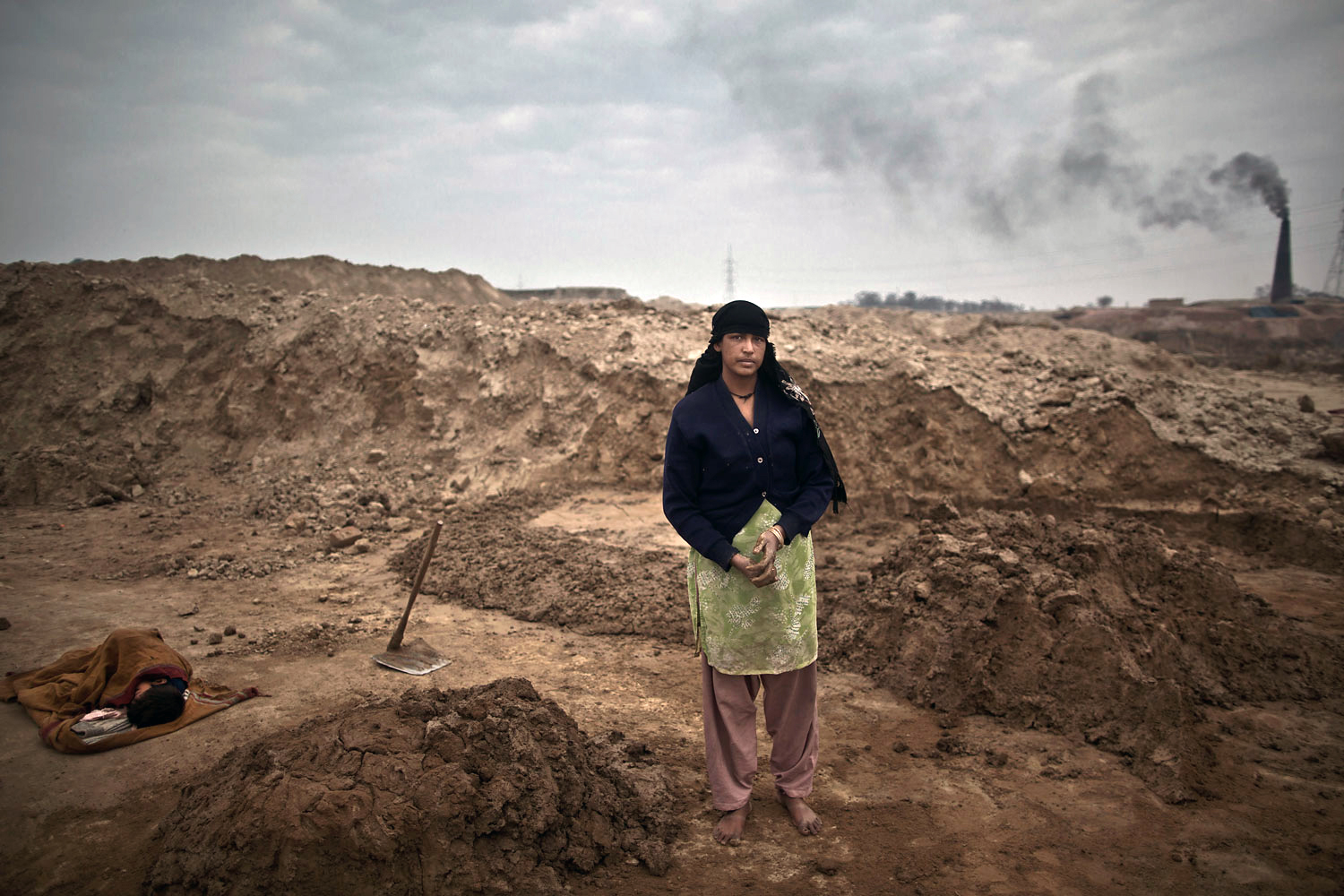With her son Adil, 6, who suffers from a fever, sleeping on the ground wrapped with a shawl, Najma Shahid, 25, a Pakistani brick factory worker, poses for a picture at the site of her work in Mandra, near Rawalpindi, Pakistan. Najma and her husband are in debt to their employer the amount of 80,000 rupees (approximately $800).