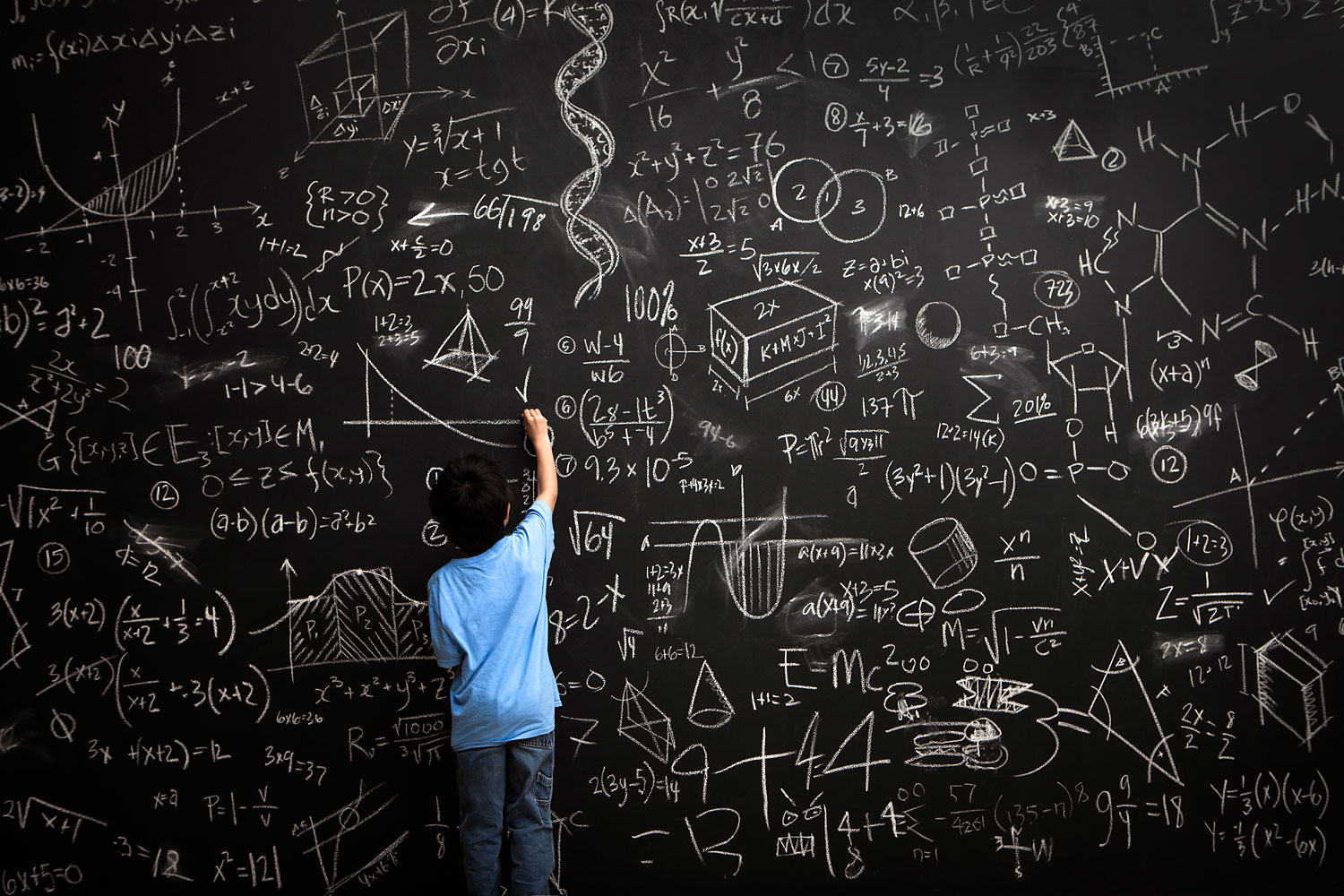 Young boy writes math equations on chalkboard
