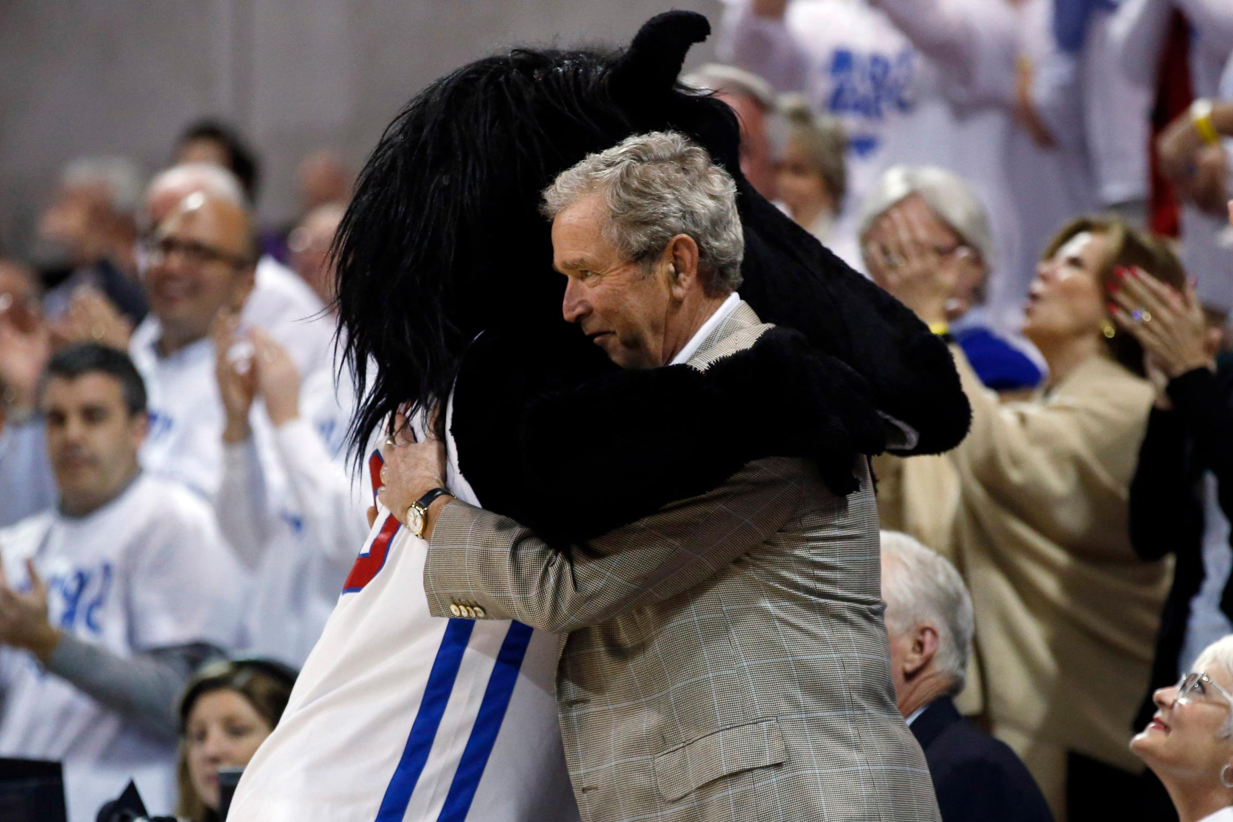 Former President George W. Bush gets a hug from SMU mascot Peruna during a break in the first of an NCAA college basketball game between SMU and Louisville on March 5, 2014, in Dallas.