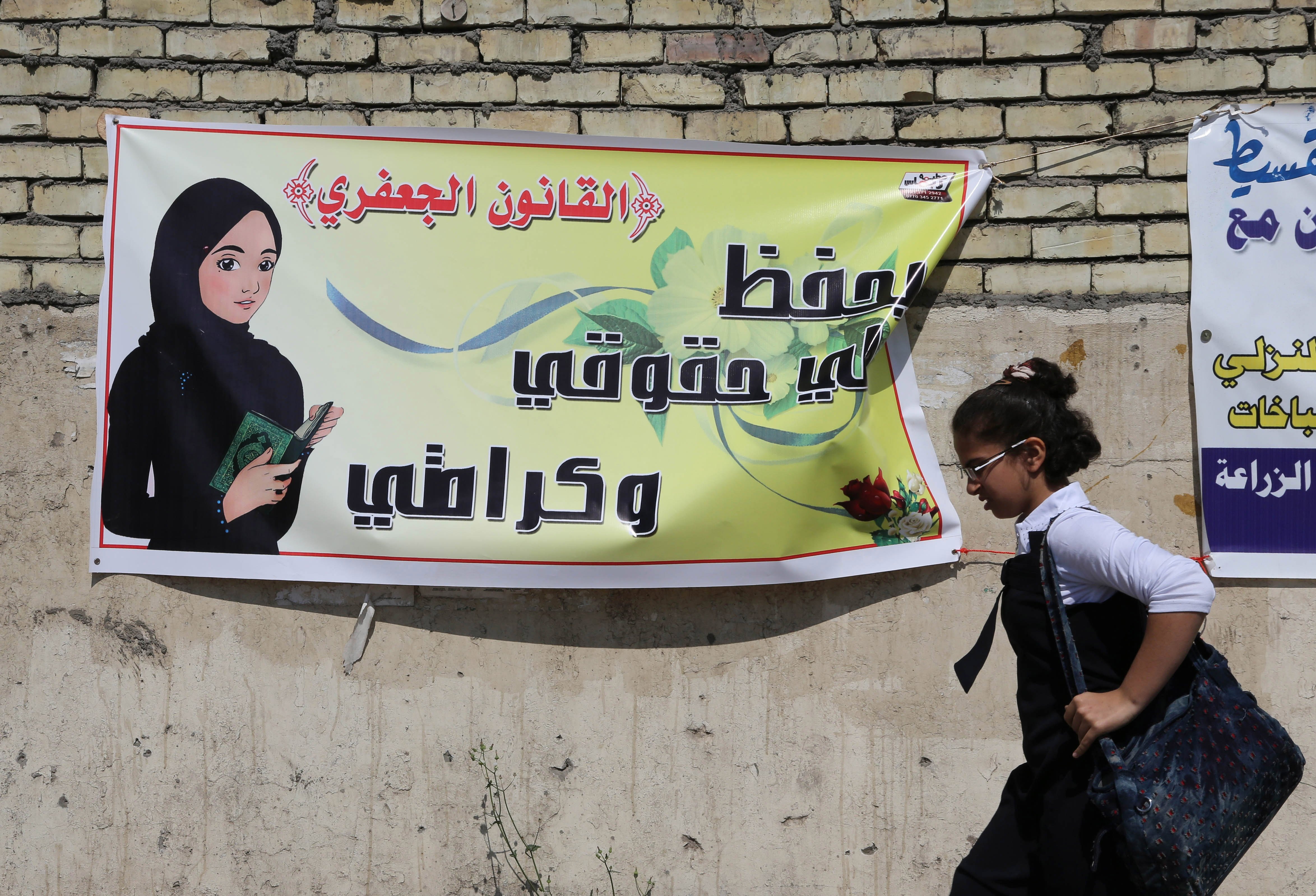 A schoolgirl passes by a banner that reads, "the Jaafari Personal Status Law saves my rights and my dignity," in Baghdad, March 13, 2014. (Karim Kadim&mdash;AP)