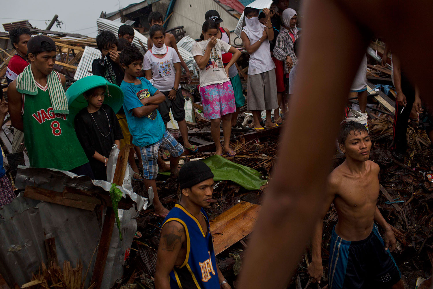 Typhoon Haiyan survivors stand in the rain and watch as people from their destroyed neighborhood search for dead bodies in the rubble in Tacloban, Philippines on November 22, 2013.