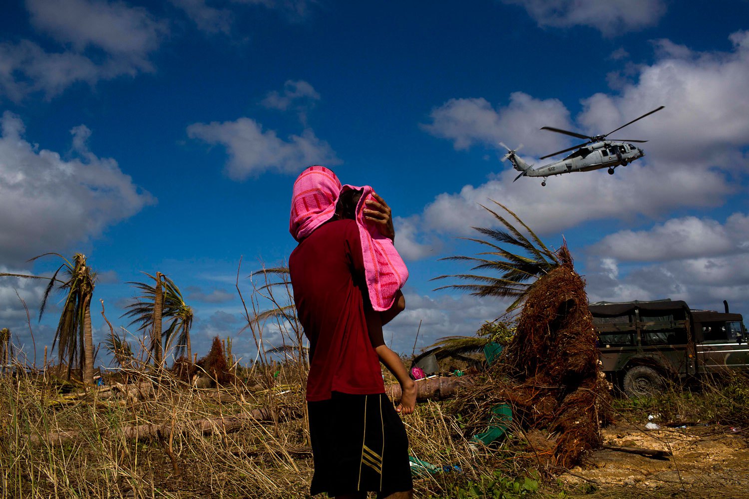 A Typhoon Haiyan survivor carries a child wrapped in a towel as he watches a helicopter landing to bring aid to the destroyed town of Guiuan, Samar Island, Philippines, November 15, 2013.
