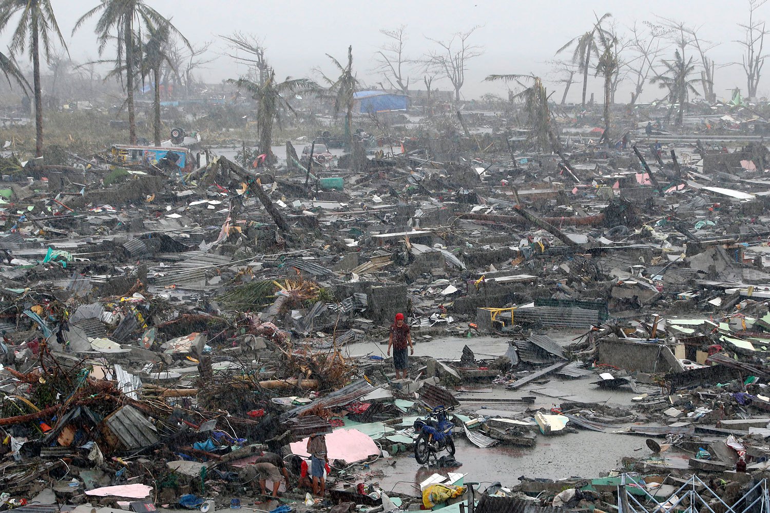 Survivors stand among debris and ruins of houses on Nov. 10, 2013, after Supertyphoon Haiyan battered the city of Tacloban, in central Philippines