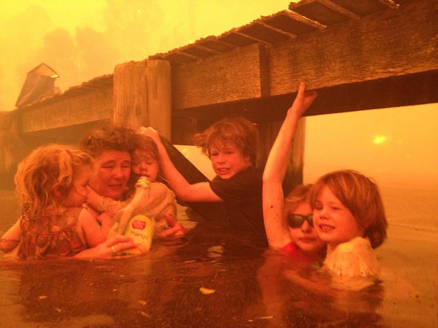 Tammy Holmes, second left, takes shelter with her grandchildren, from left, Charlotte Walker, 2, Esther Walker, 4, Liam Walker, 9, Matilda, 11, and Caleb Walker, 6, under a jetty as a wildfire rages nearby in Dunalley, Australia, Jan. 4, 2013.