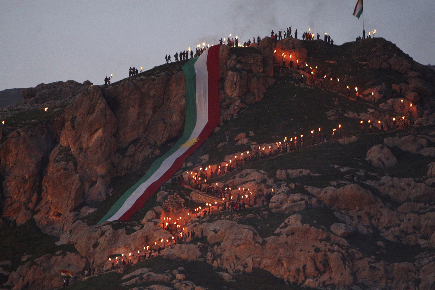 Iraqi Kurdish people carry fire torches up a mountain where a giant flag of Iraq's autonomous Kurdistan region is laid, as they celebrate Newroz Day, a festival marking their spring and new year, near Dahuk
