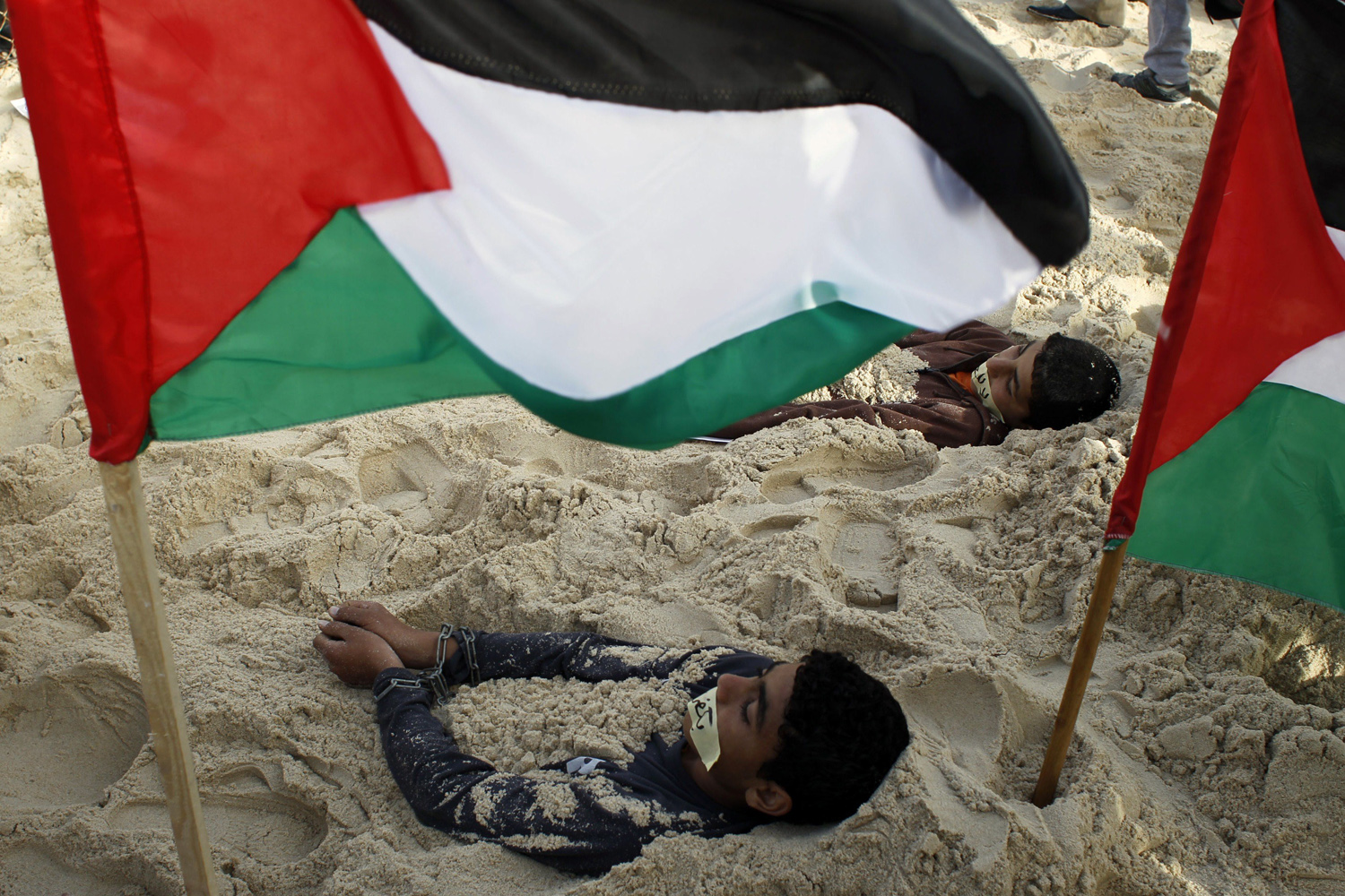Mar. 7, 2014. Palestinian children lie in the sand with their hands clasped next to their national flags during a rally against the siege on the impoverished Hamas-run Gaza Strip in the coastal town of Rafah.