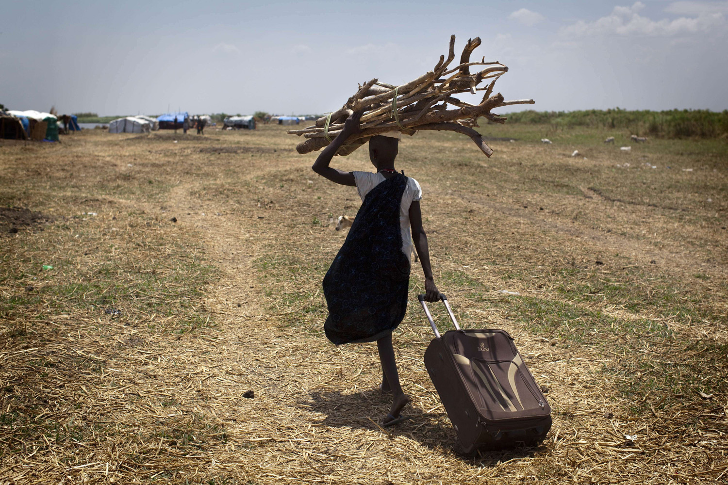 Mar. 5, 2014. A South Sudanese woman walks with wood to reinforce her house in an isolated makeshift IDP camp for Dinka ethnic group placed in an island between Bor and Minkamman.