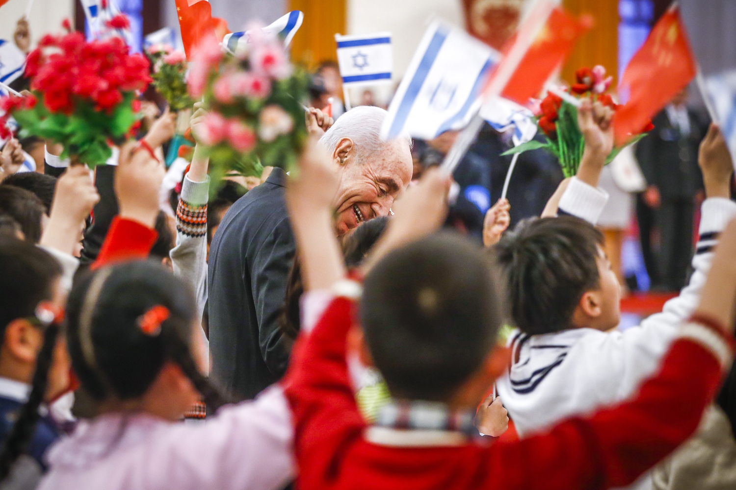 Israeli President Shimon Peres, center, talks to school children holding Chinese and Israeli national flags during a welcoming ceremony hosted by Chinese President Xi Jinping (not pictured) inside the Great Hall of the People in Beijing on April 8, 2014.