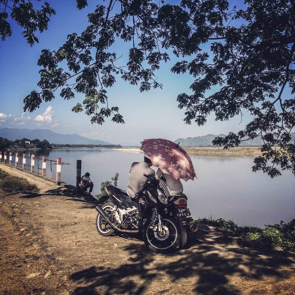 A teenage couple huddles together on motorbikes under their umbrella next to the Irrawaddy River in Myitkyina, Myanmar on November 1, 2013.