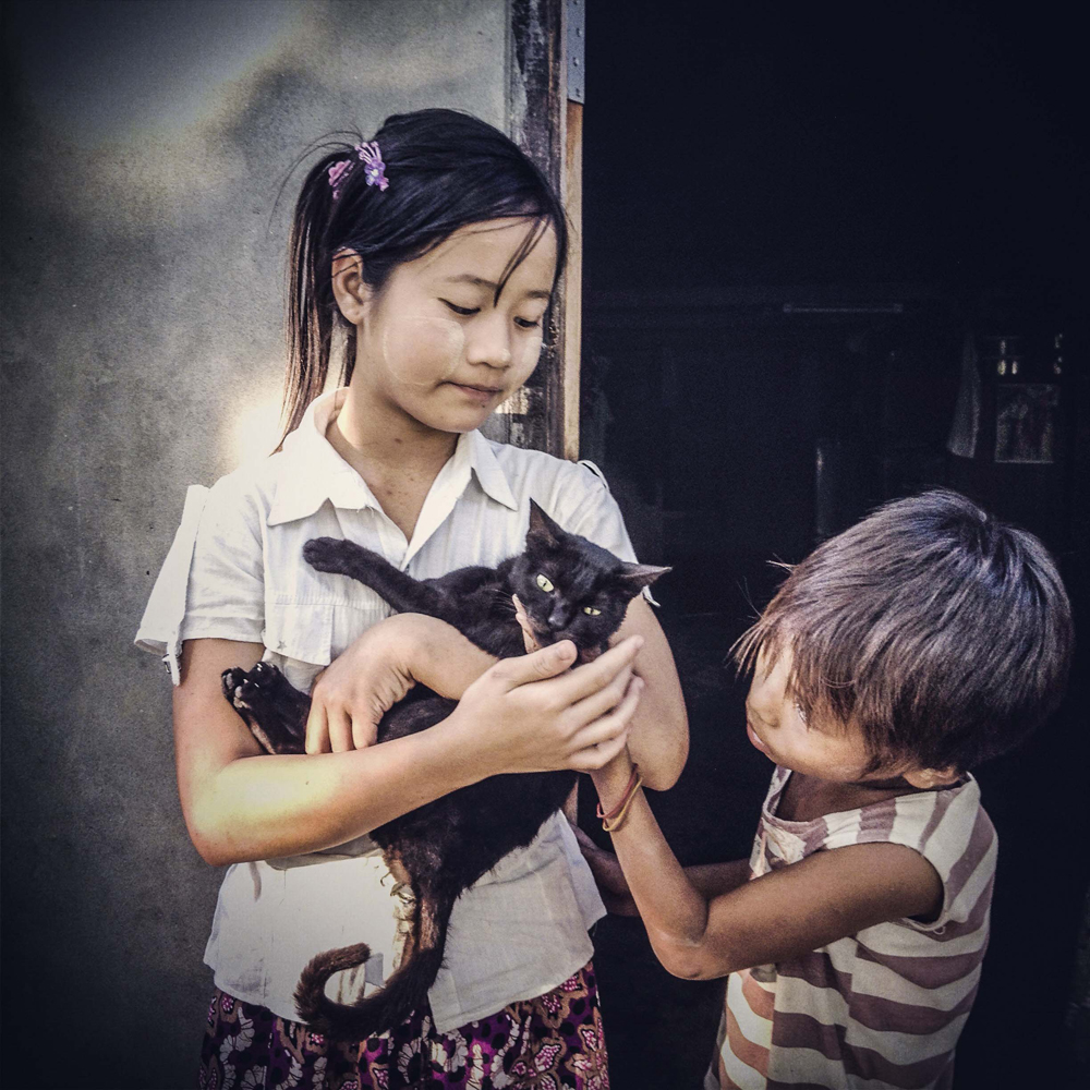 A young girl and boy play with a cat outside of a small school on the outskirts of Pathein, Myanmar in the Ayeyarwady Division of the Irrawaddy Delta on February 4, 2014.