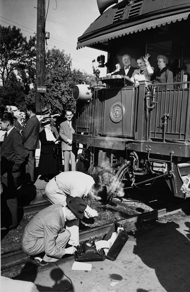 Reporters work away as President Harry Truman, his wife Bess and their daughter Margaret wave from a train during a whistle-stop at Pocatello, Idaho, in 1948.