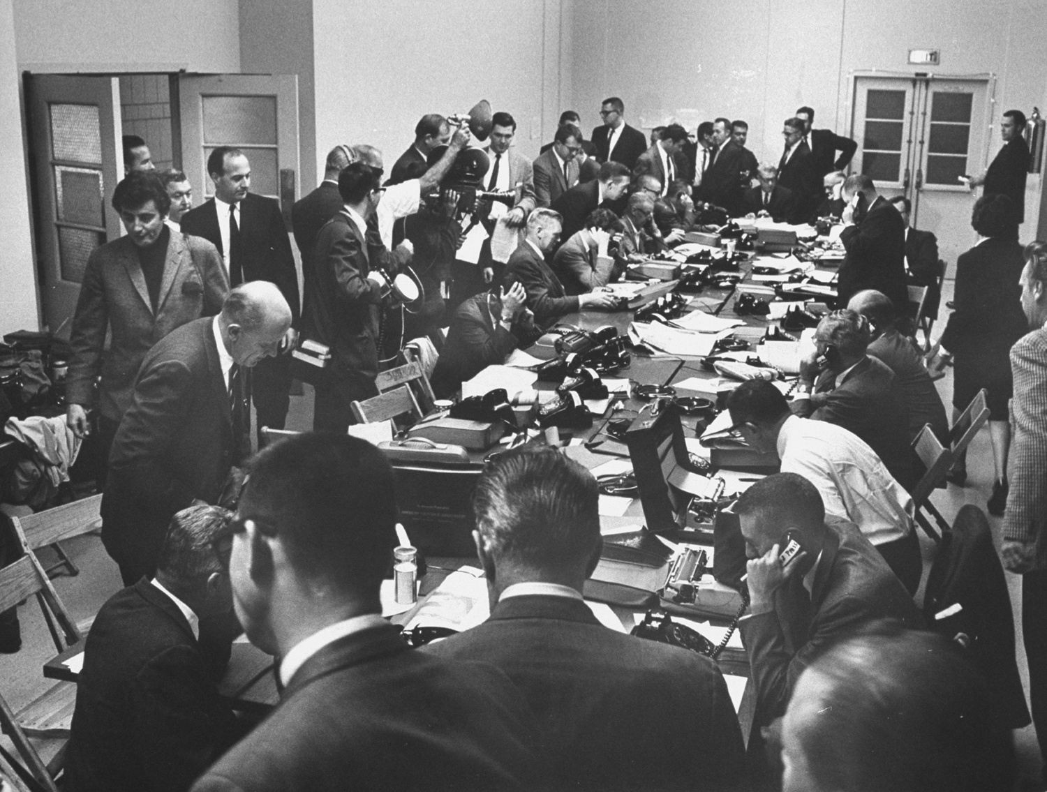 Reporters and photographers (incl. Harry Benson, at left in black shirt) waiting for information on President Lyndon B. Johnson's condition after a gall bladder operation at Bethesda Naval Hospital, 1965.