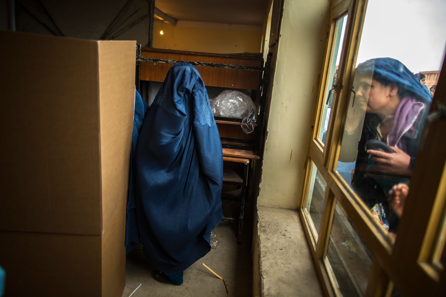 An Afghan woman looks through a window as another is about to cast her ballot at a polling station in Mazar-i-Sharif