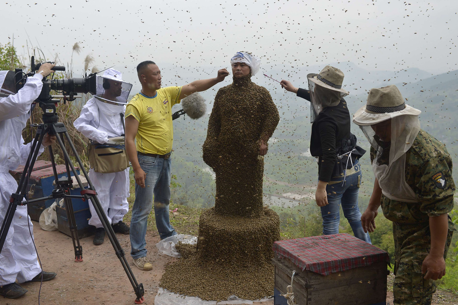 Assistants use burning incense and cigarettes to drive away from the face of She Ping, a 34-year-old beekeeper, during an attempt to cover his body with bees, in Chongqing municipality April 9, 2014.