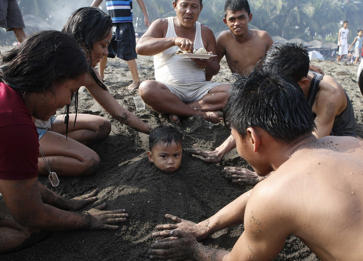 A family helps bury a boy in sand at a beach to celebrate Easter Sunday, near Manila Bay in Cavite province April 20, 2014.