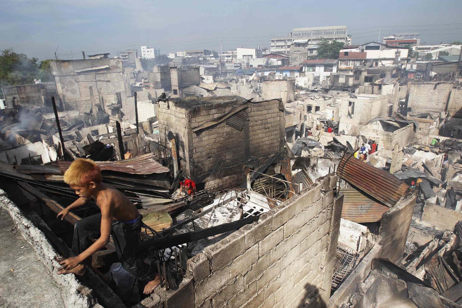 A boy climbs out of a charred shanty as he collects reusable materials after a fire razed through a slum area in Caloocan City, Metro Manila
