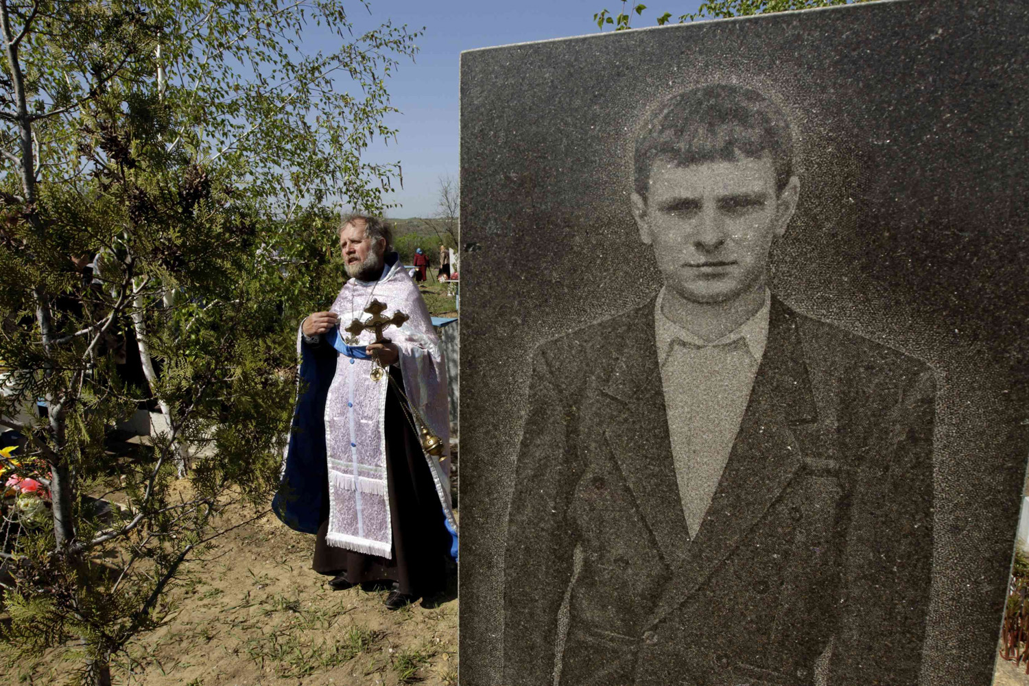 An Orthodox priest walks past a portrait of a man on a grave, as he conducts a service in a cemetery near the village of Zimogorie