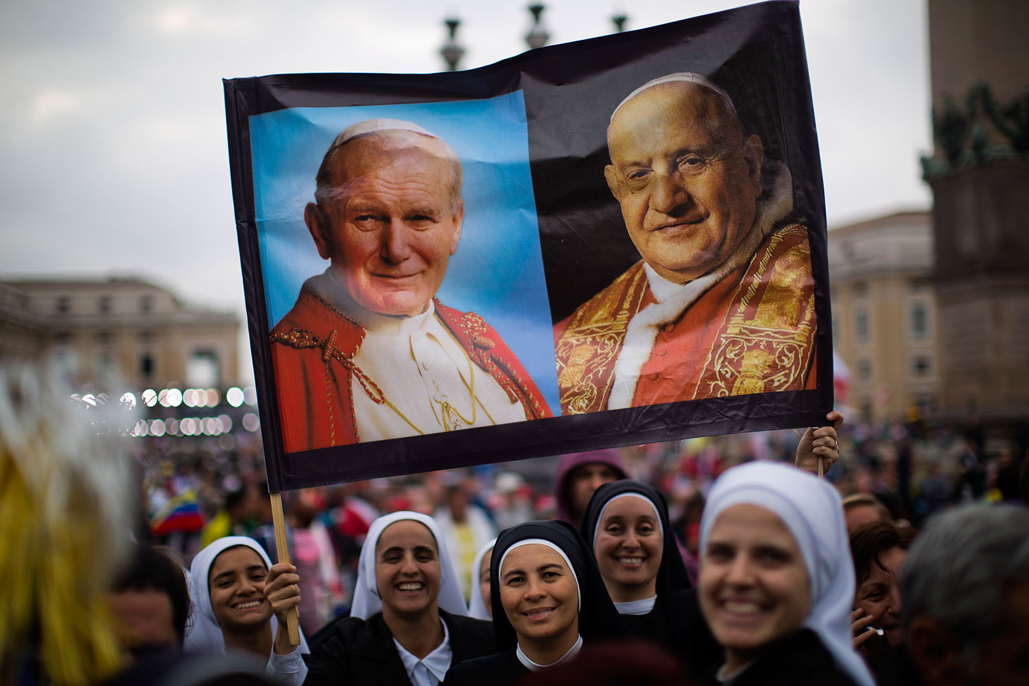 Nuns hold up a poster with portraits of  Pope John Paul II, left, and John XXIII, in St. Peter's Square at the Vatican, April 27, 2014.