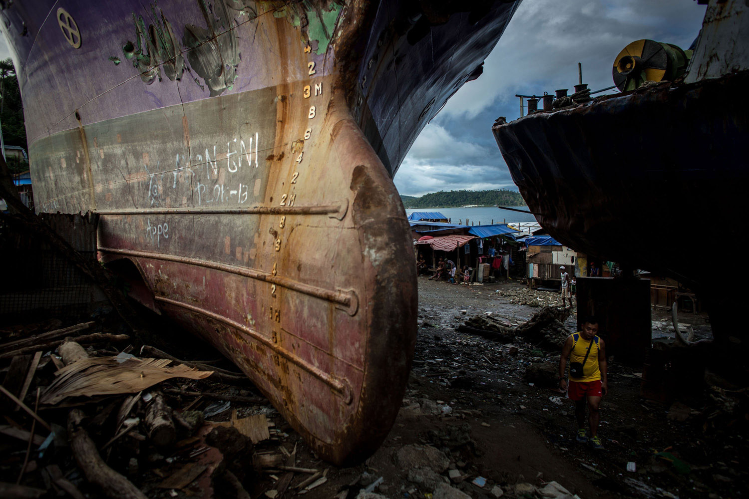 Apr. 18, 2014. A man walks through a gap between three large ships that were grounded by Typhoon Haiyan in Tacloban, Leyte, Philippines. People continue to rebuild their lives five months after Typhoon Haiyan struck the coast  on November 8, 2013, leaving more than 6000 dead and many more homeless.