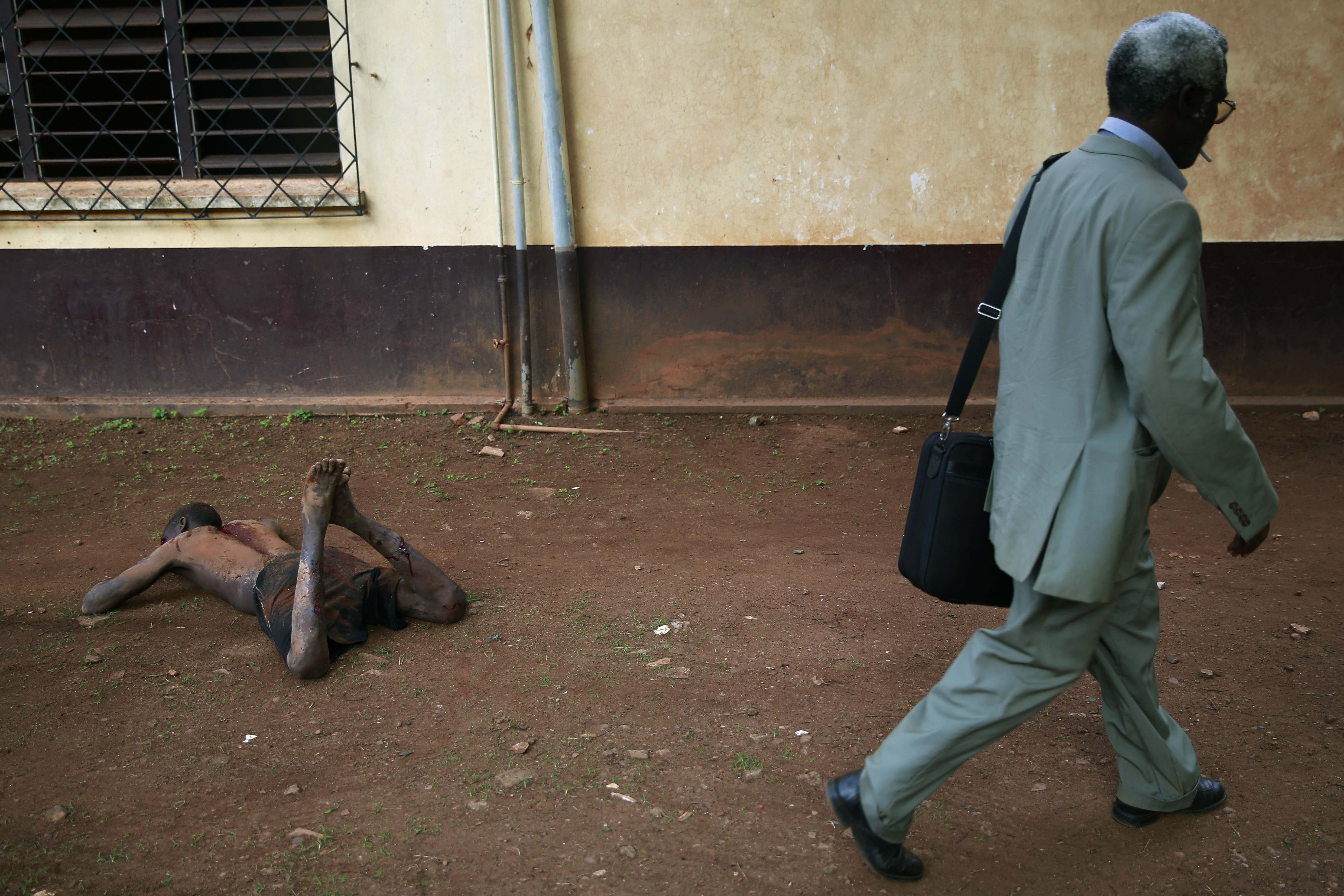 Apr. 18, 2014. A man walks by a man accused of being a thief by civil servants at the Work Inspection office, as he lays in pain after being attacked by a man with a machete and sticks,  in plain view of others, in Bangui, Central African Republic.