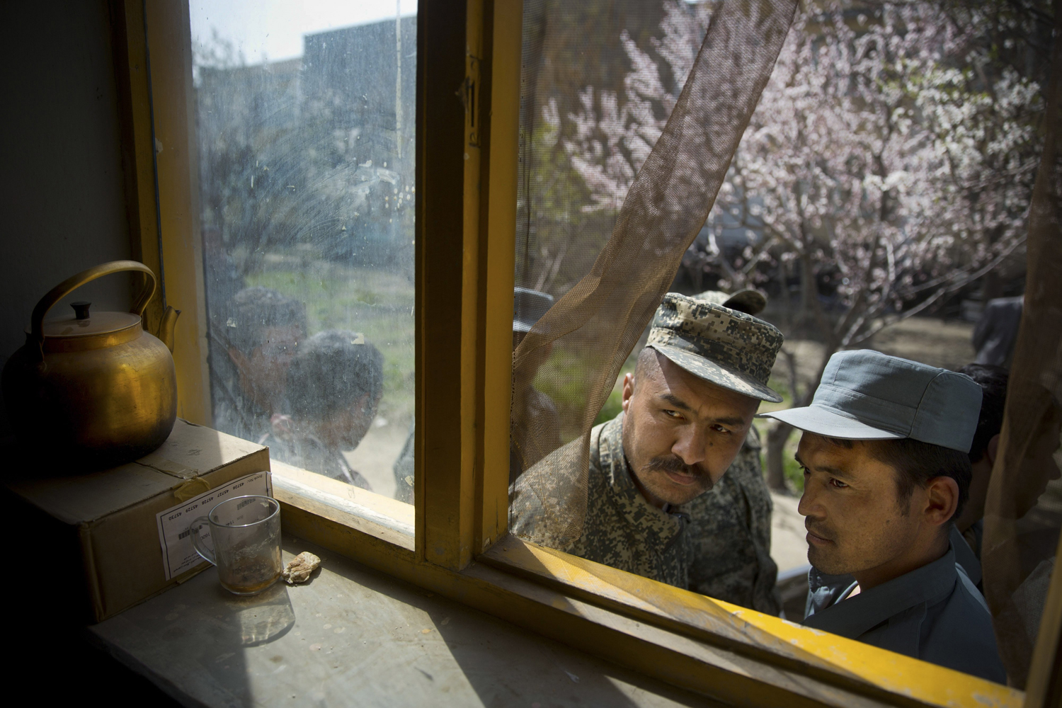 Apr. 1, 2014. An Afghan soldier, left, and a police man peek through a window as they queue with others to get their registration card on the last day of voter registration for the upcoming presidential elections outside a school in Kabul, Afghanistan.
