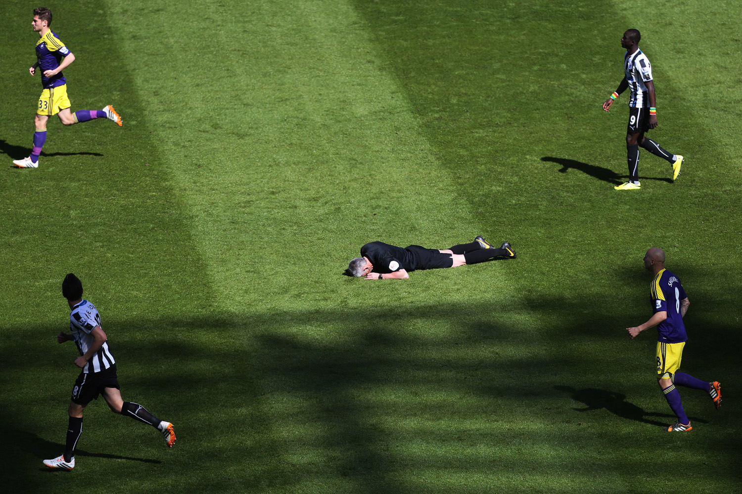Referee Chris Foy, center, is laid on the pitch after being struck by a ball to the face during the English Premier League soccer match between Newcastle United and Swansea City at St James' Park, Newcastle, England, April 19, 2014.