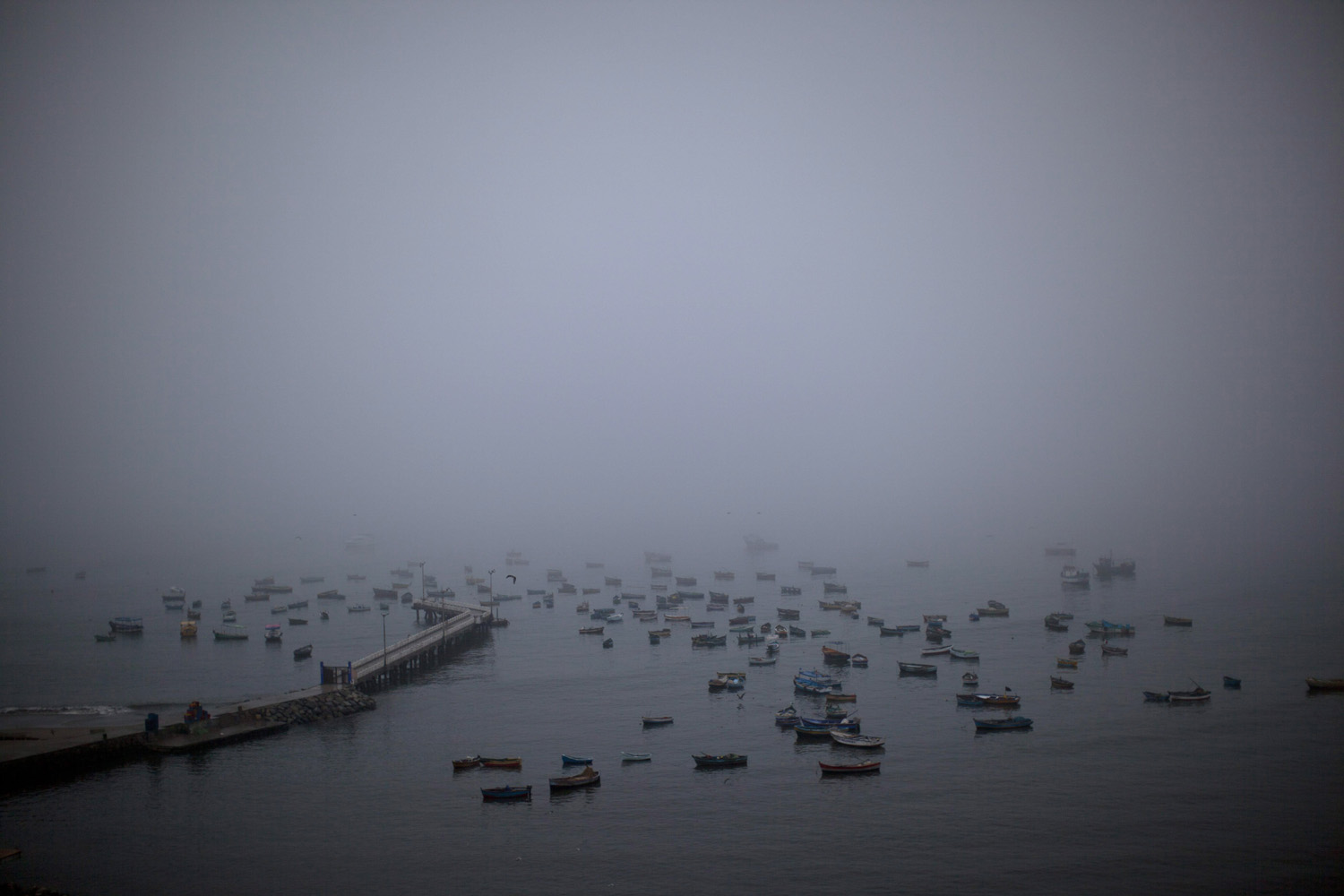 Apr. 2, 2014. Morning fog lifts at the Chorrillo dock in the Pacific Ocean, revealing small scale fishing boats in Lima, Peru.