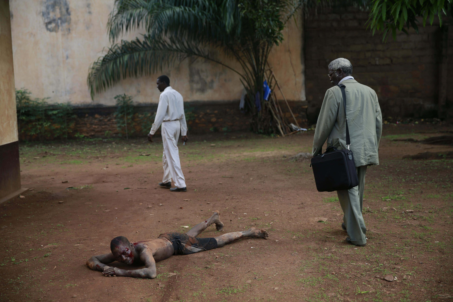 A man walks by Kevin, a man accused of being a thief by civil servants at the Work Inspection office, as he lays in pain after being attacked by a man with a machete and sticks,  in plain view of others, in Bangui, Central African Republic, April 18, 2014.