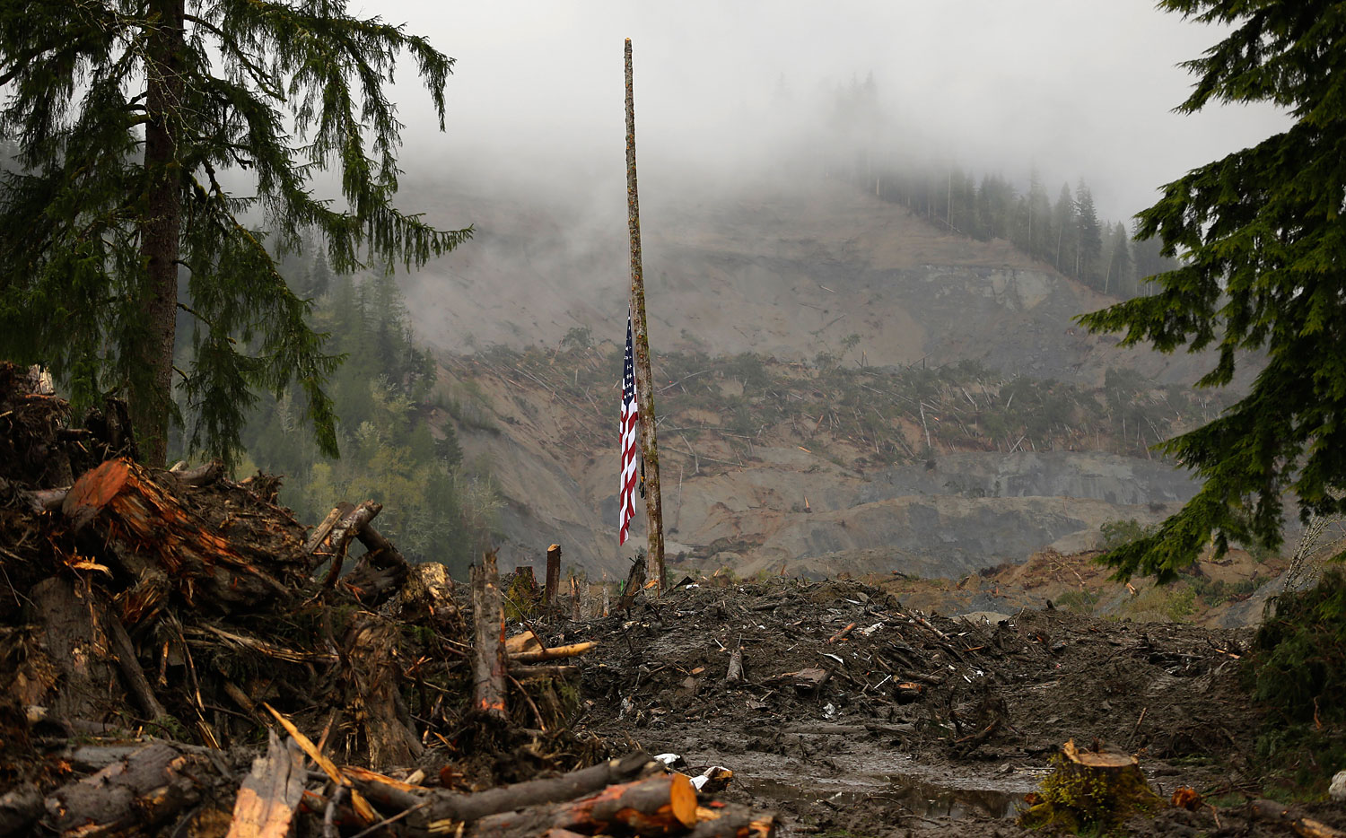 A flag rests at half staff on a cedar pole, Wednesday, April 16, 2014, with the face of the massive deadly mudslide that hit the community of Oso, Wash. on March 22, 2014 behind it. (Ted S. Warren—AP)
