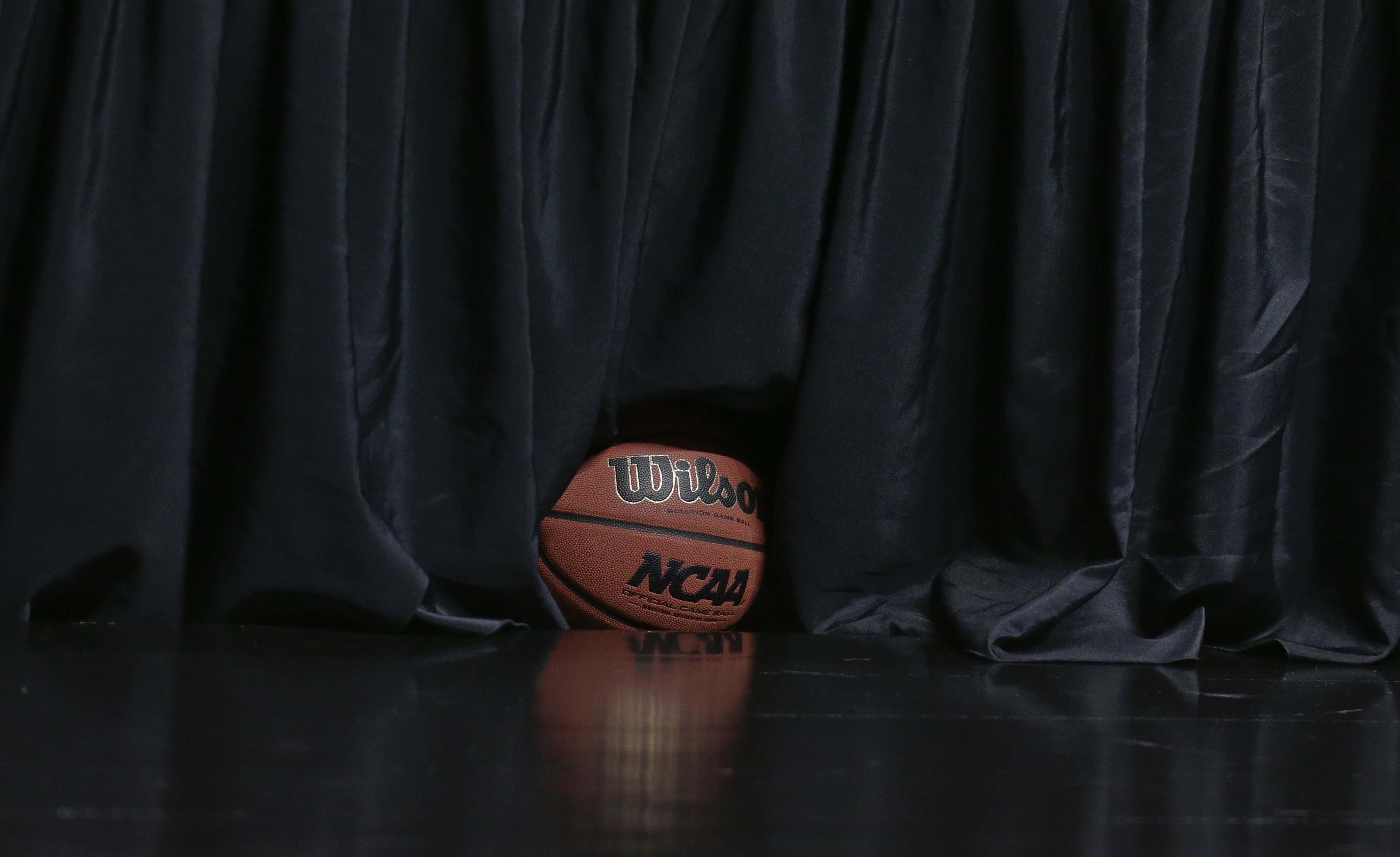 A basketball sits under a curtain, court side, before a third round game between UCLA and Stephen F. Austin at the NCAA college basketball tournament, March 23, 2014, in San Diego.