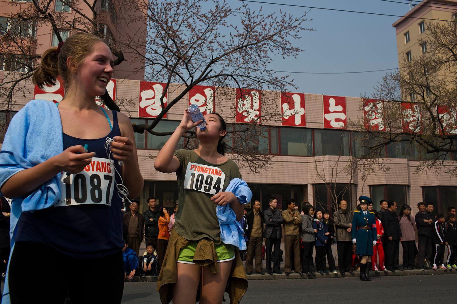 Tourists who competed in the shorter distance segments of the marathon, rest at the end of the race on April 13, 2014. From left are Harriet Harrper-Jones, England, and Allie Wu, Taiwan. The sign behind them reads  Long Live the Shining Revolutionary Tradition of Our Party.