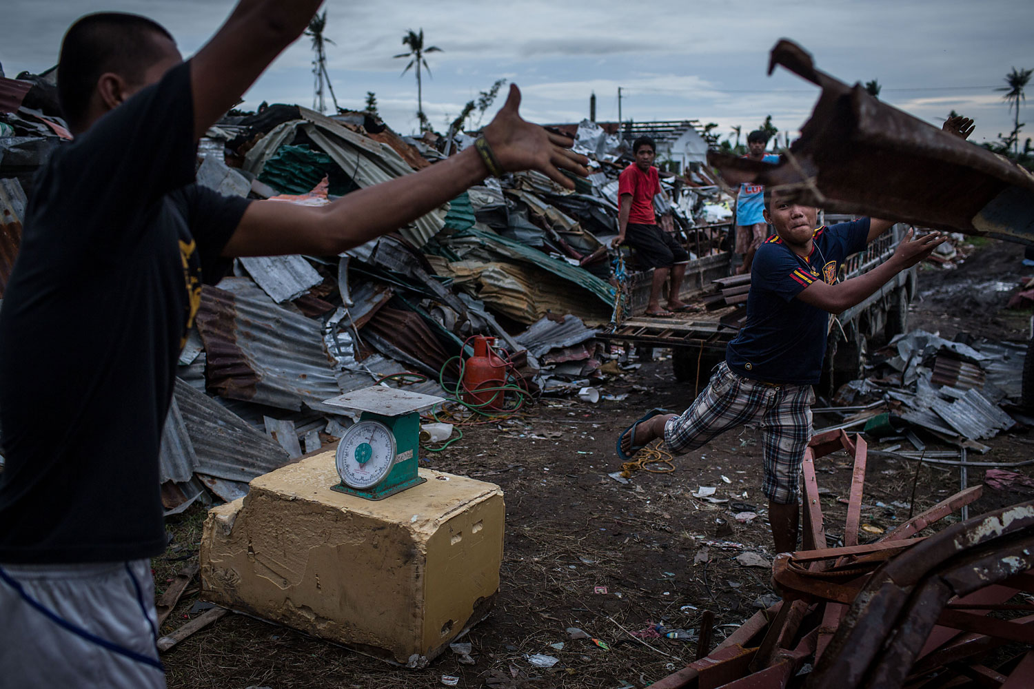 Workers at a junkyard throw scrap metal on a pile after weighing it on April 16, 2014 in Tacloban.