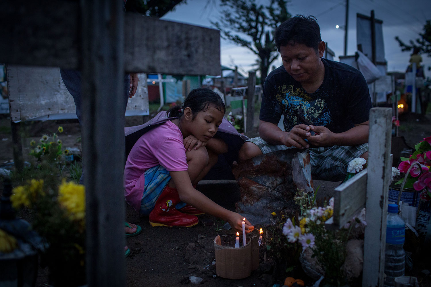 Jonna Lizette C. Modesto lights candles at the gravesite of her 5-year old brother John Reyneud C. Modesto watched on by her father Anastacio S. Modesto III at the makeshift mass grave site at San Joaquin Parish on April 16, 2014 in Tacloban.
