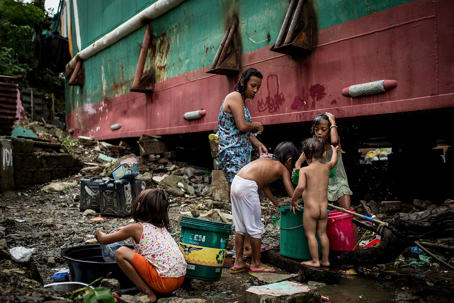 A family washes and cleans clothes next to the hull of a large ship grounded by Typhoon Haiyan on April 18, 2014 in Tacloban.