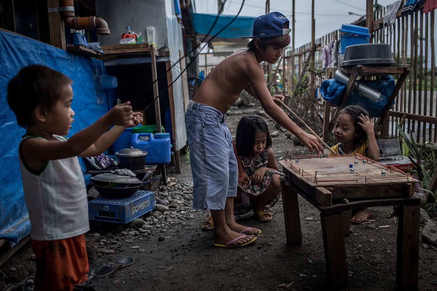 Kids watch on as a boy plays pool with marbles on a makeshift pool table in a temporary bunk house complex on April 16, 2014 in Tacloban.