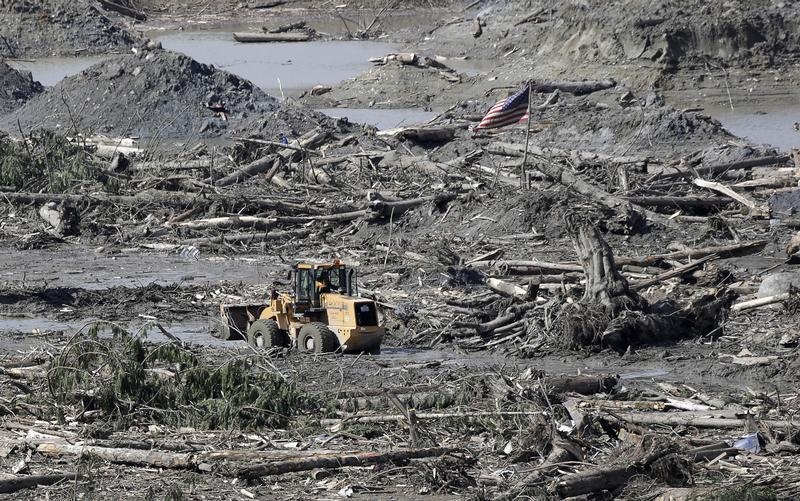 A piece of heavy equipment moves past an American flag as search work continues in the mud and debris from a massive mudslide that struck Oso near Darrington, Washington
