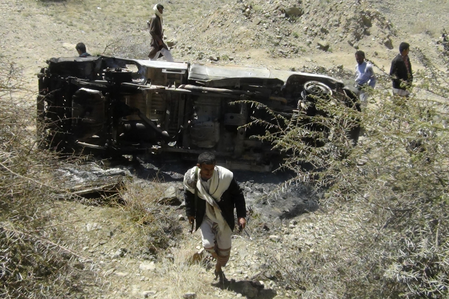 People inspect the wreckage of a car hit by an air strike in the central Yemeni province of al-Bayda