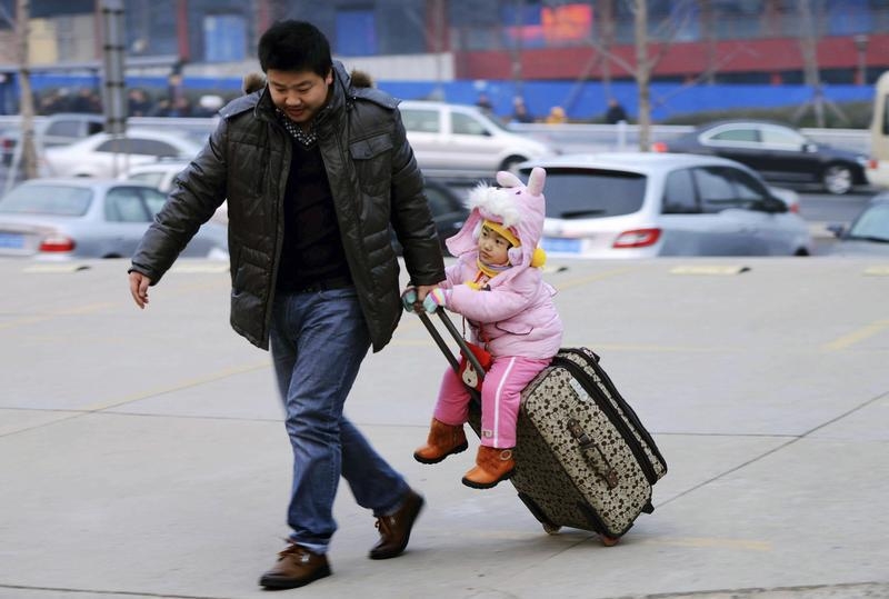 A man drags a suitcase with a girl sitting on it at a long-distance bus terminus in Qingdao, Shandong province