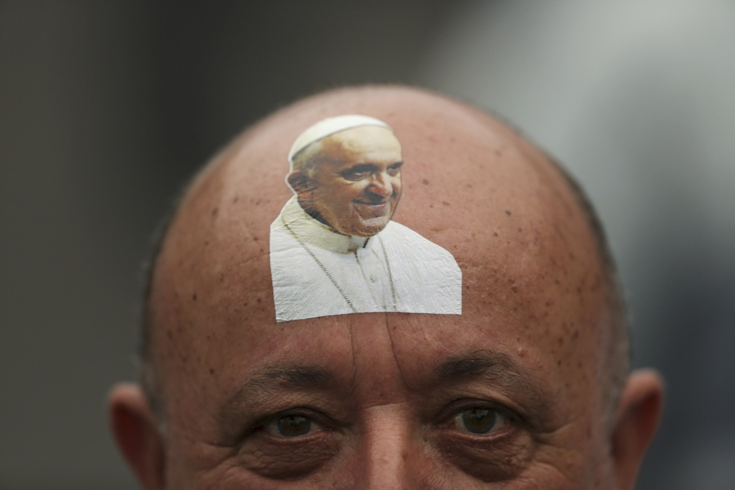 Catholic faithful with sticker bearing an image of Pope Francis on his forehead looks on while waiting for the Pope to arrive in Copacabana beach in Rio de Janeiro