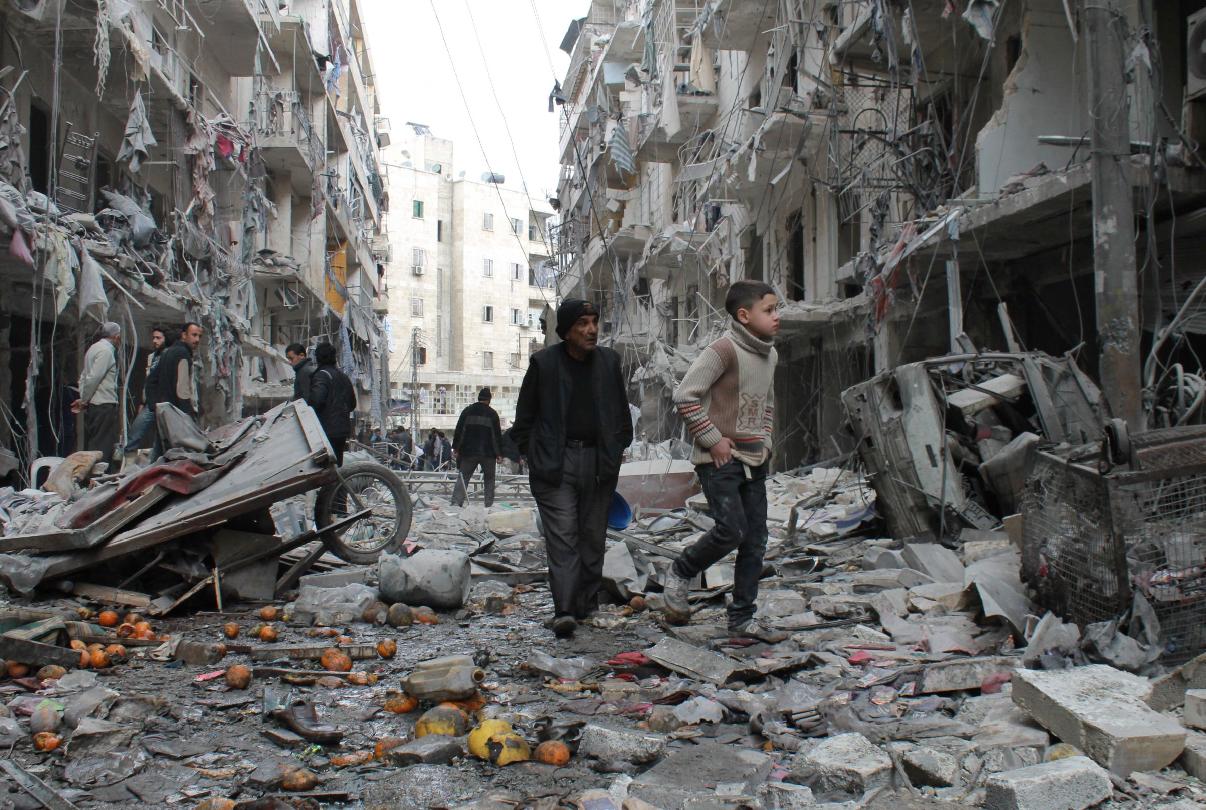 An elderly Syrian man and a child walk amidst debris in a residential block reportedly hit by an explosives-filled barrel dropped by a government forces helicopter on March 18, 2014 in Aleppo.