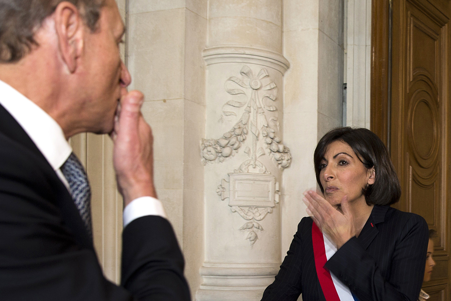 From right, The new mayor of Paris, socialist Anne Hidalgo, wearing her tricolour mayoral sash, and former mayor, socialist Bertrand Delanoe, blow a kiss to each other as Delanoe leaves the Paris city hall during the inaugural session of the newly elected council on April 5, 2014.