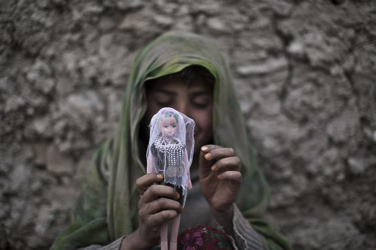 Apr. 3, 2014. An Afghan girl sits on the ground dressing her doll while playing in an alley in Kabul, Afghanistan.