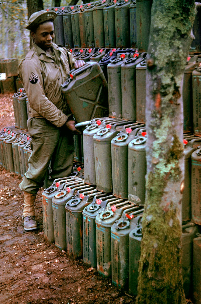 An American corporal stacks cans of gasoline in preparation for the upcoming invasion of France, Stratford-upon-Avon, England, May 1944.