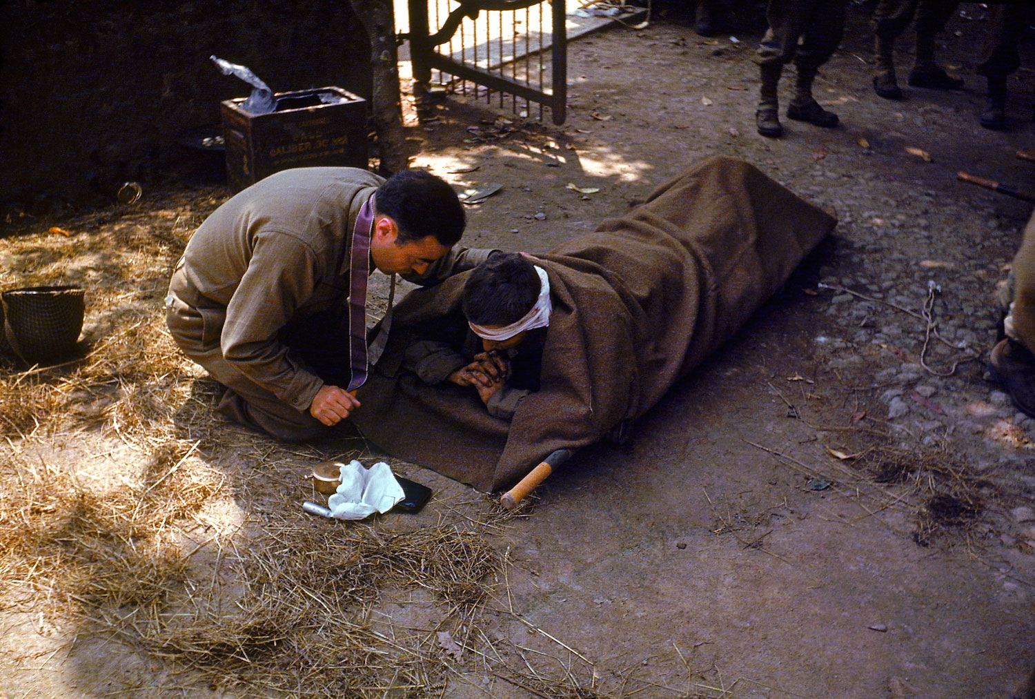 An American Army chaplain kneels next to a wounded soldier in order to administer the Eucharist and Last Rites, France, 1944.
