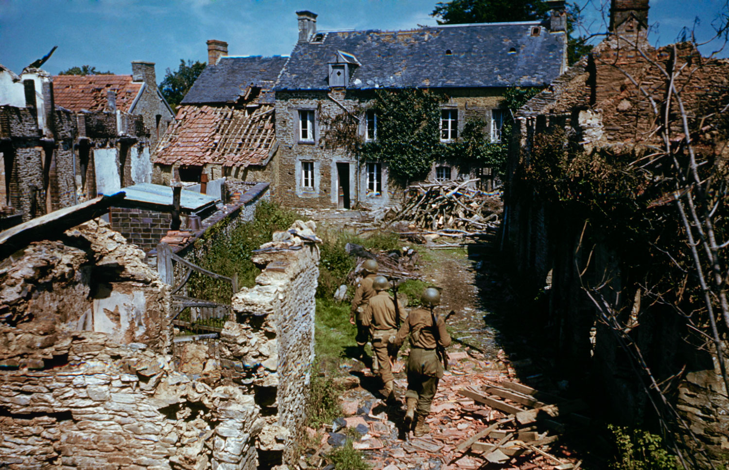 GIs search ruined homes in western France after D-Day.