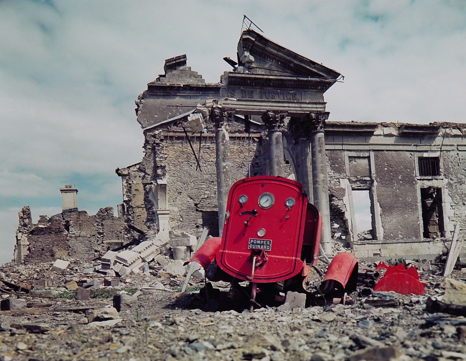 View of the ruins of the Palais de Justice in the town of St. Lo, France, summer 1944. The red metal frame in the foreground is what's left of an obliterated fire engine.